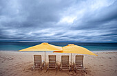 Liegestühle und Sonnenschirme am Strand an einem bewölkten Tag; Turks- und Caicosinseln, Westindische Inseln