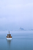 Fishing boat and the town of Mont Lois in the fog; Mont Lois, Gaspe Peninsula, Quebec, Canada