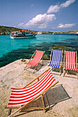 Cruise boat sails by a Mediterranean shoreline with deck chairs; Comino Island, Malta