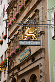 Sign Hanging From A Building With Blossoming Flowers In Window Planter Boxes; Rothenburg Ob Der Tauber Bavaria Germany