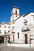 Weißes Kirchengebäude mit einer Uhr und einem Kreuz auf einem Turm vor blauem Himmel; Grazalema Andalusien Spanien