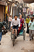 Ein Mann fährt mit einer Frau in einer Fahrradrikscha eine schmale Straße entlang; Ludhiana, Punjab, Indien