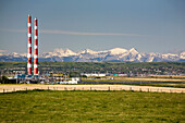 Zwei rot und weiß gestreifte Schornsteine eines Gaswerks mit schneebedeckten Bergen im Hintergrund und blauem Himmel; Alberta Kanada