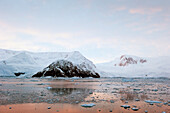 The Coastline Reflected In The Tranquil Water At Sunset; Antarctica