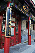 Rote Säulen und Fassade an einem Gebäude mit goldenen chinesischen Schriftzeichen; Peking China