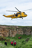 Ein Rettungshubschrauber fliegt über den Arbeitern am Boden; Northumberland England