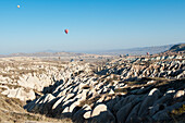 Hot Air Balloons Fill The Blue Sky Over A Rugged Landscape; Nevsehir Turkey
