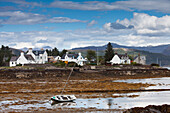A Boat Lays In The Shore At Low Tide With Houses Along The Coastline; Plockton Highlands Scotland