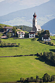 Kirche mit Zwiebelkuppelturm auf einer Wiese mit Bergen und Tälern im Hintergrund; Bozen, Dolomiten, Südtirol, Italien
