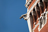 Gargoyle on edge of brick castle tower and blue sky; Milano, Lombardia, Italy