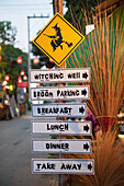 Thailand, Post with various signs for coffee shop and sign with witch on broom; Pai