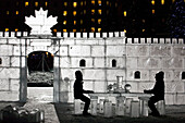 Canada, Alberta, Silhouette of man and woman sitting at ice table in ice castle; Lake Louise