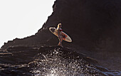 Portugal, Algarve, Carrapateira, Distant View Of Female Surfer With Surfboard Standing On Rock; Playa Do Amado