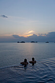 Zwei Menschen am Rande eines Infinity Pools genießen den Sonnenuntergang; Ko Samui, Thailand