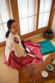 A Woman Sits Wearing A Lovely Traditional Hanbok In Bokchon Hanok Village; Seoul, South Korea