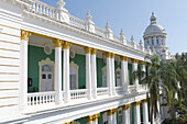 Ein Gebäude mit weißen Säulen, Geländern und Balustern und einem grünen Innenkorridor