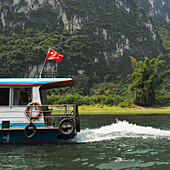 A Boat With A Chinese Flag Traveling Down Li River; Guilin, Guangxi, China