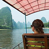 A Woman Rides In A Covered Boat Down The Li River; Guilin, Guangxi, China