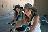 Zwei Mädchen tragen Sonnenhüte und sitzen auf Fahrrädern; China