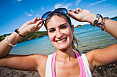 Eine junge Frau posiert mit Sonnenbrille entlang der Küste von Urupukapuka Island; Neuseeland
