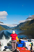 Ein Reisender genießt die landschaftlich reizvolle Fahrt über den Lake Manapouri zum Doubtful Sound; Neuseeland