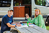 Ein älteres Ehepaar sitzt an einem Picknicktisch und isst zu Abend mit ihrem Wohnmobil im Hintergrund auf dem West Canada Creek Campingplatz; Polen, New York, Vereinigte Staaten von Amerika