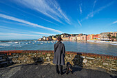 Eine Frau und ihr Hund stehen am Ufer des Hafens und schauen auf die Küste; Sestri Levante, Leguria, Italien