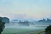 Landschaftlicher Blick auf nebliges Ackerland am Morgen mit Windrad im Hintergrund, Oberpfalz, Bayern, Deutschland