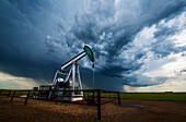 Pumpenheber, Ölquelle, auf einem Feld mit stürmischem Himmel, Kanadische Prärien, Saskatchewan, Kanada