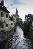 Wohnhäuser entlang des Moldaukanals mit dem Turm des Schlosses Cesky Krumlov im Hintergrund, Cesky Krumlov, Tschechische Republik.