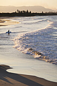 Silhouette eines Surfers, der die Wellen beobachtet, die am Strand von Byron Bay in New South Wales, Australien, ans Ufer schlagen