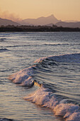 Pastellfarbene Wellen, die bei Sonnenuntergang am Strand von Byron Bay in New South Wales, Australien, auf das Ufer treffen