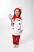 Kleines Mädchen als Koch verkleidet, der einen Schneebesen hält