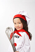 Kleines Mädchen als Koch verkleidet, einen Schneebesen haltend