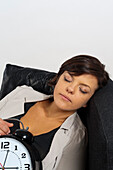 Portrait of Mid-Adult Woman Sleeping on Sofa and holding Alarm Clock