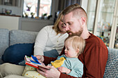Parents with baby with down syndrome reading a book on sofa