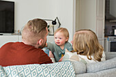 Parents playing with smiling baby Parents with baby with down syndrome reading a book on sofa on sofa in living room