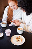 Junge Frauen telefonieren und schauen sich soziale Medien im Cafe an