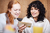 Junge Frauen telefonieren und lachen über ein Meme im Cafe