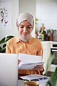 Smiling woman with hijab checking bills at home