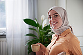 Portrait einer lächelnden Frau mit Hidschab beim Kaffee trinken