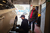 Mechaniker in der Werkstatt wechselt Reifen am Auto und spricht mit Kundin