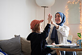 Mother wearing hijab helping son doing homework and doing high five
