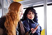 Freundinnen sitzen zusammen im Bus und schauen auf ihr Handy