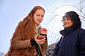 Female friends looking at cell phone outdoors with sun in the background