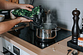 Woman's hands putting vegetables in saucepan