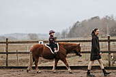 Girl horseback riding with female instructor walking along her