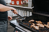 Man's hand holding tongs and grilling meat
