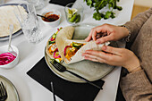 Person wrapping Mexican tortilla with various toppings