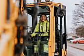 Portrait of smiling female road worker operating excavator